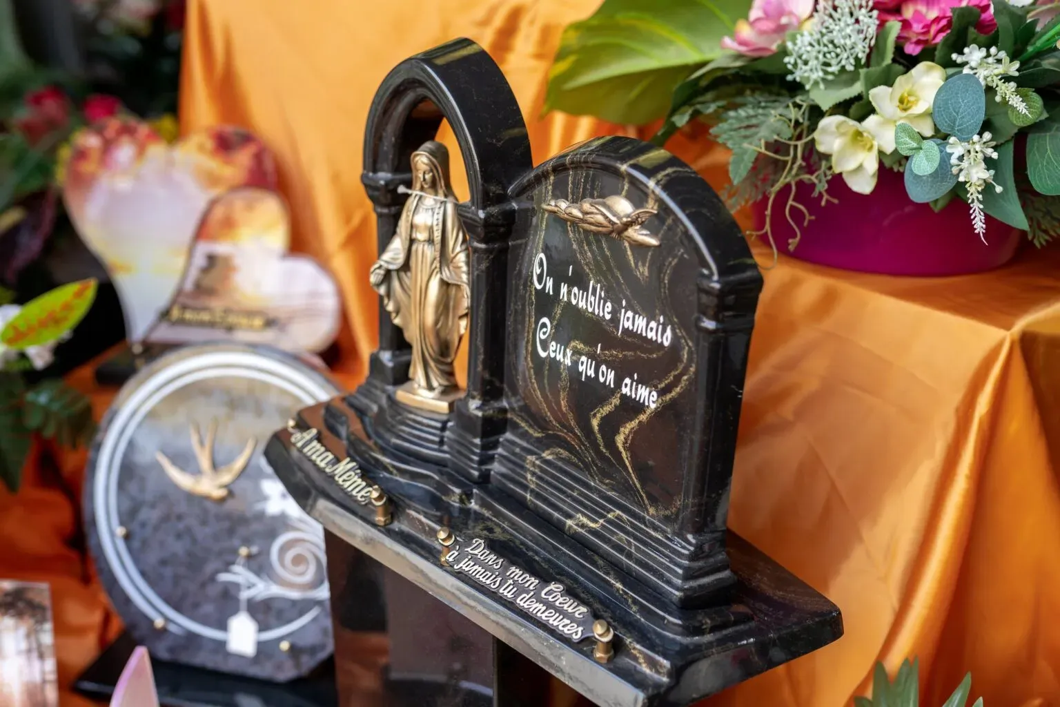 Plaque mortuaire en marbre noir avec statuette religieuse et dorures.