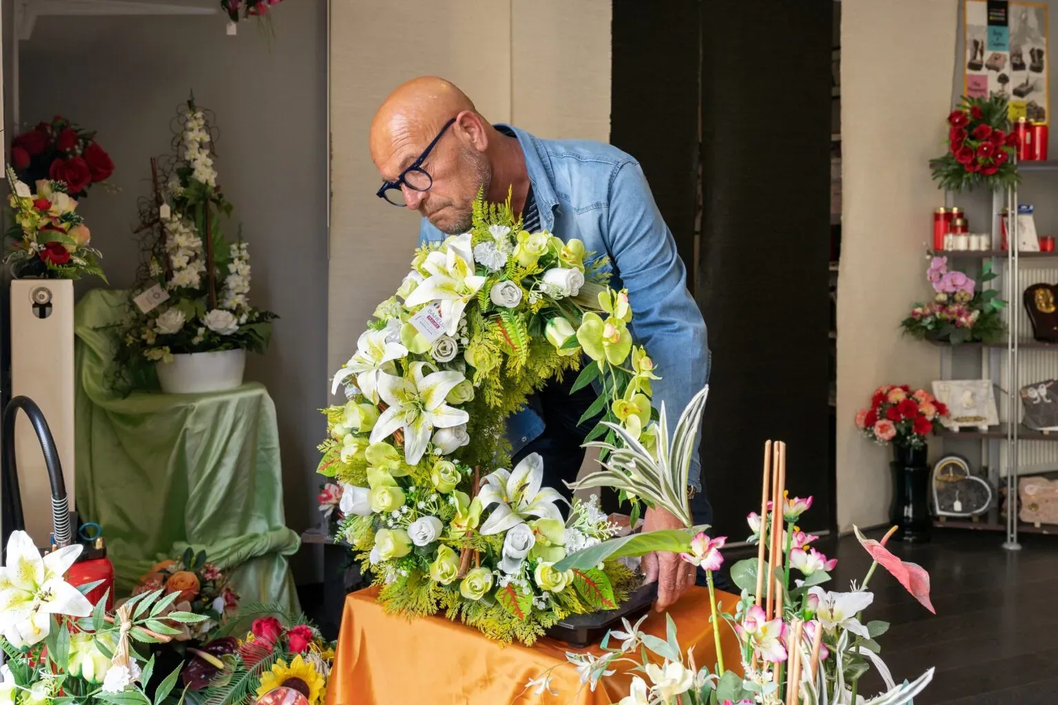 Artisan fleuriste préparant une couronne mortuaire dans son magasin.